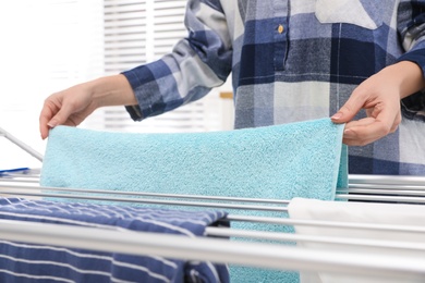 Photo of Young woman hanging clean laundry on drying rack at home, closeup