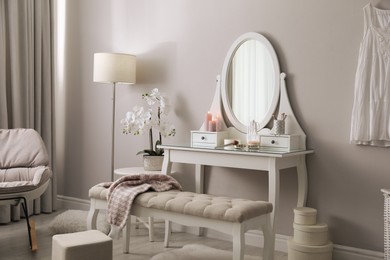 Wooden dressing table with decorative elements and makeup products in room. Interior design