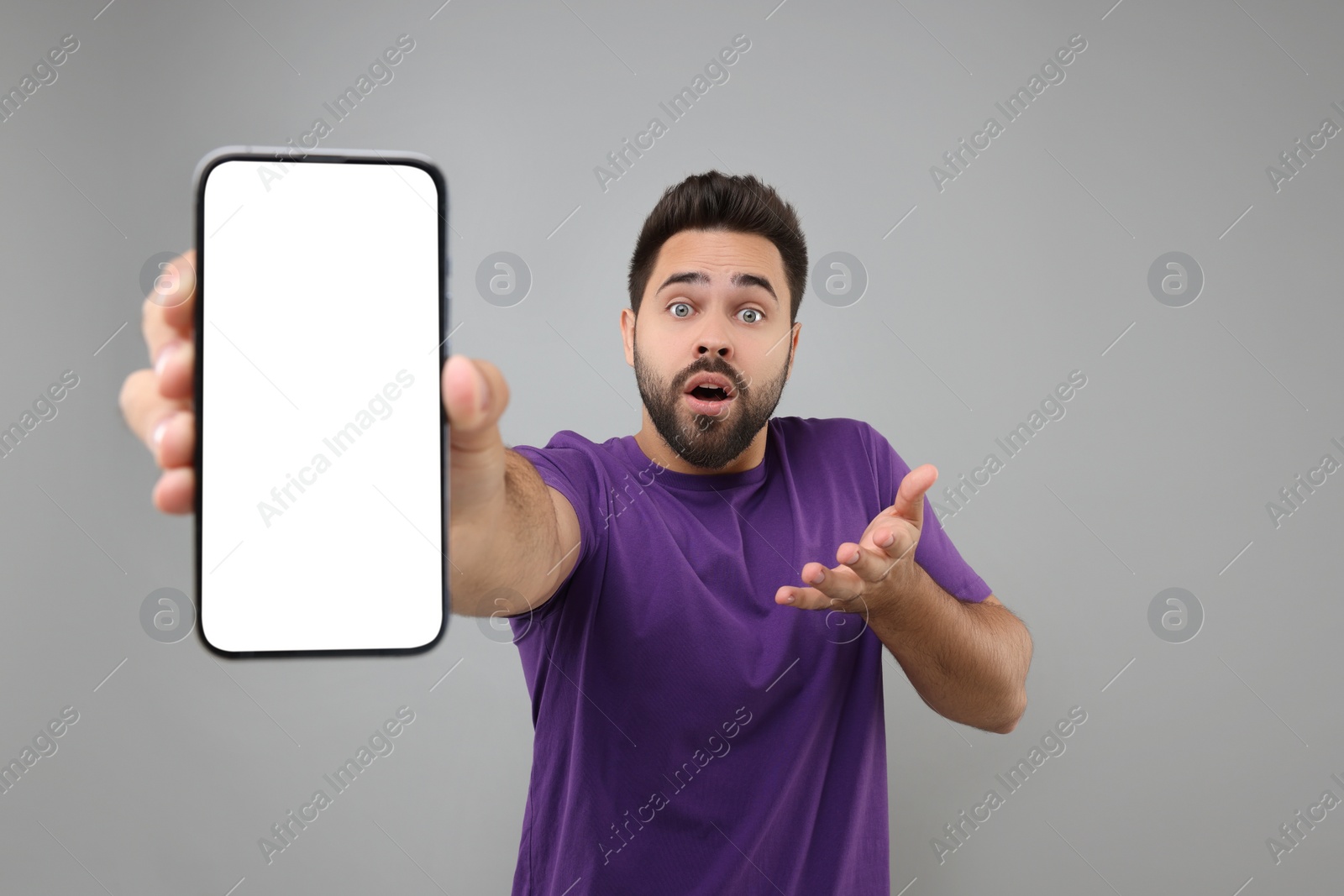 Photo of Surprised man showing smartphone in hand on light grey background