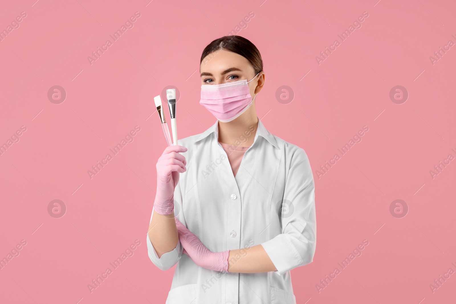 Photo of Cosmetologist with cosmetic brushes on pink background