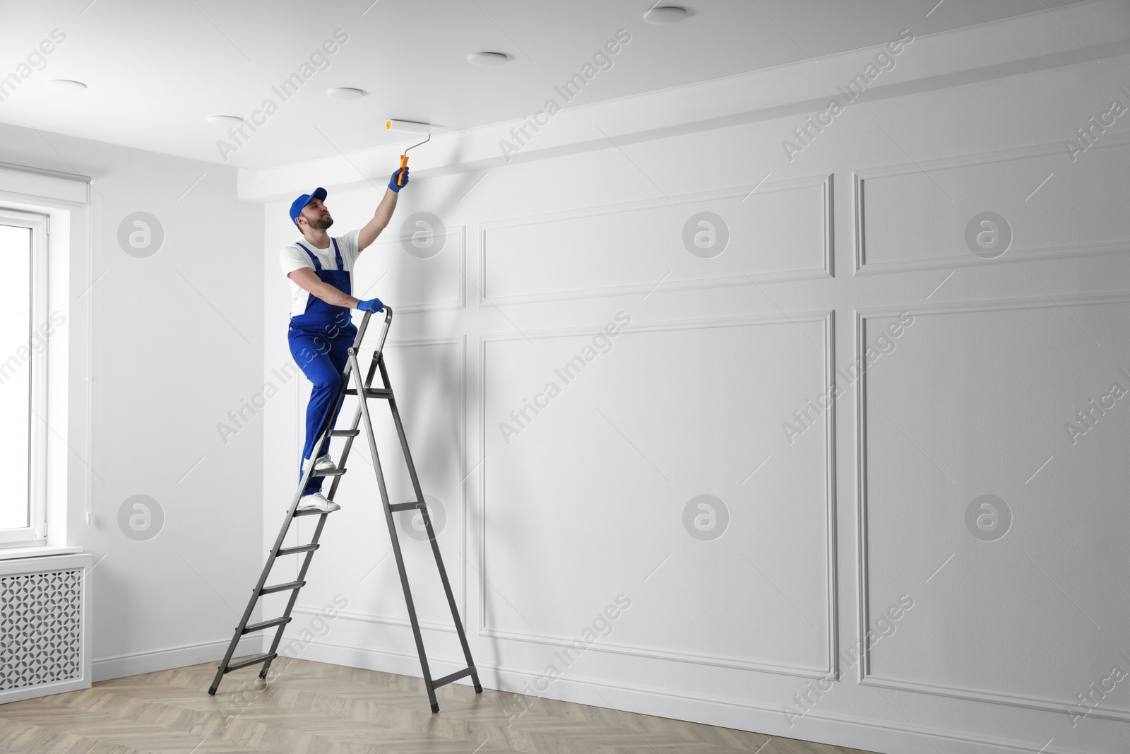 Photo of Handyman painting ceiling with white dye indoors, space for text