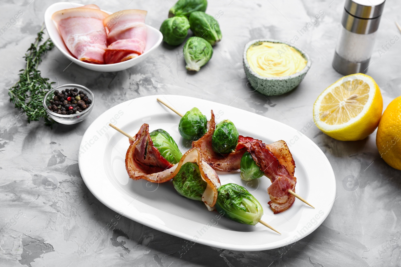 Photo of Skewers with Brussels sprouts and bacon in plate on grey table