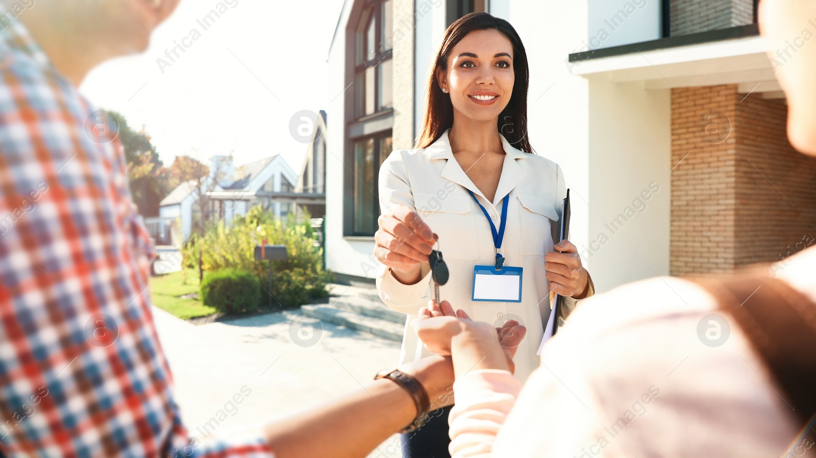 Photo of Real estate agent giving house keys to young couple outdoors