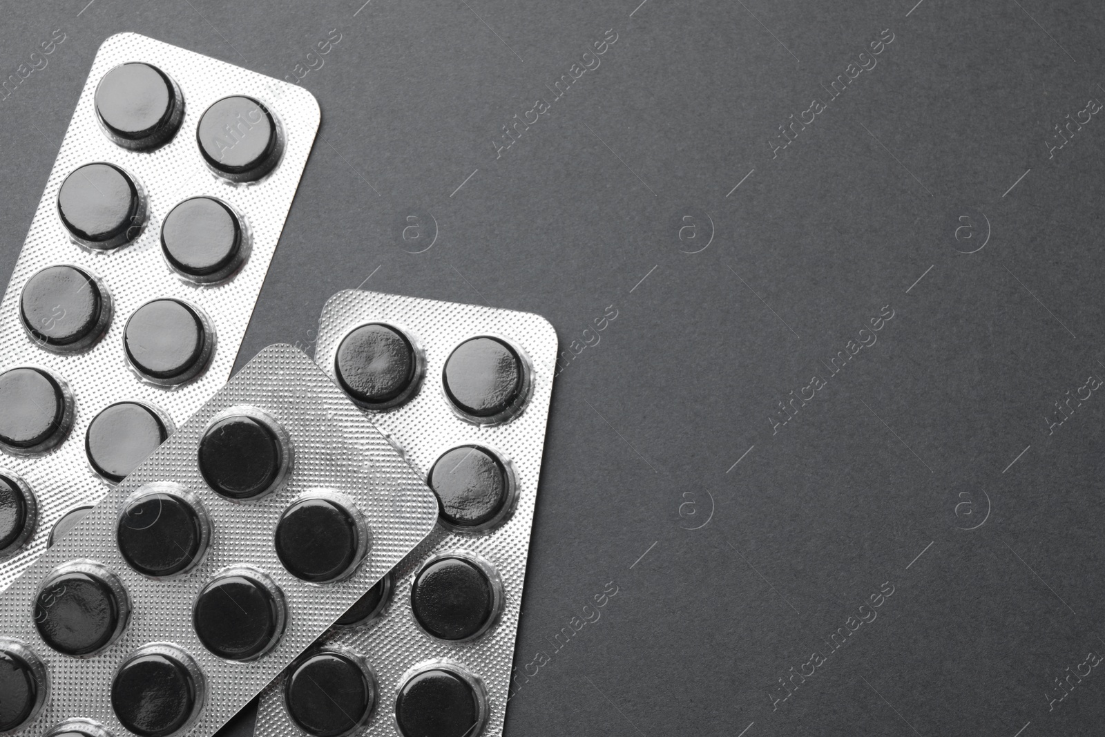 Photo of Activated charcoal pills in blisters on black background, flat lay with space for text. Potent sorbent