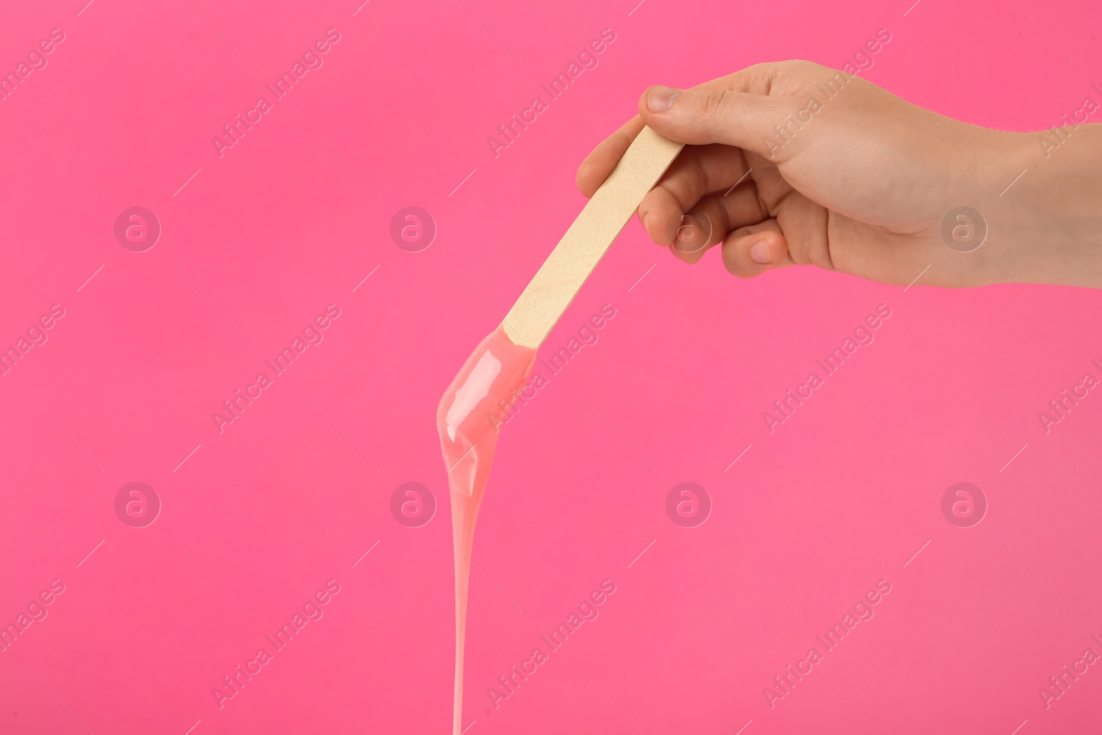 Photo of Woman holding spatula with hot depilatory wax on pink background, closeup