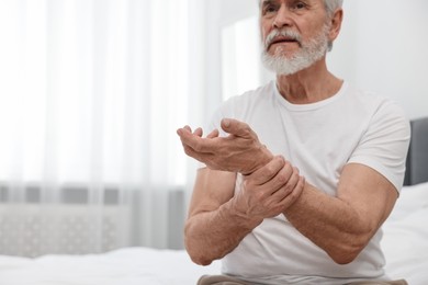 Arthritis symptoms. Man suffering from pain in wrist on bed at home, space for text