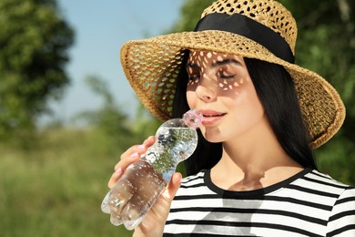 Photo of Beautiful young woman drinking water outdoors. Refreshing drink