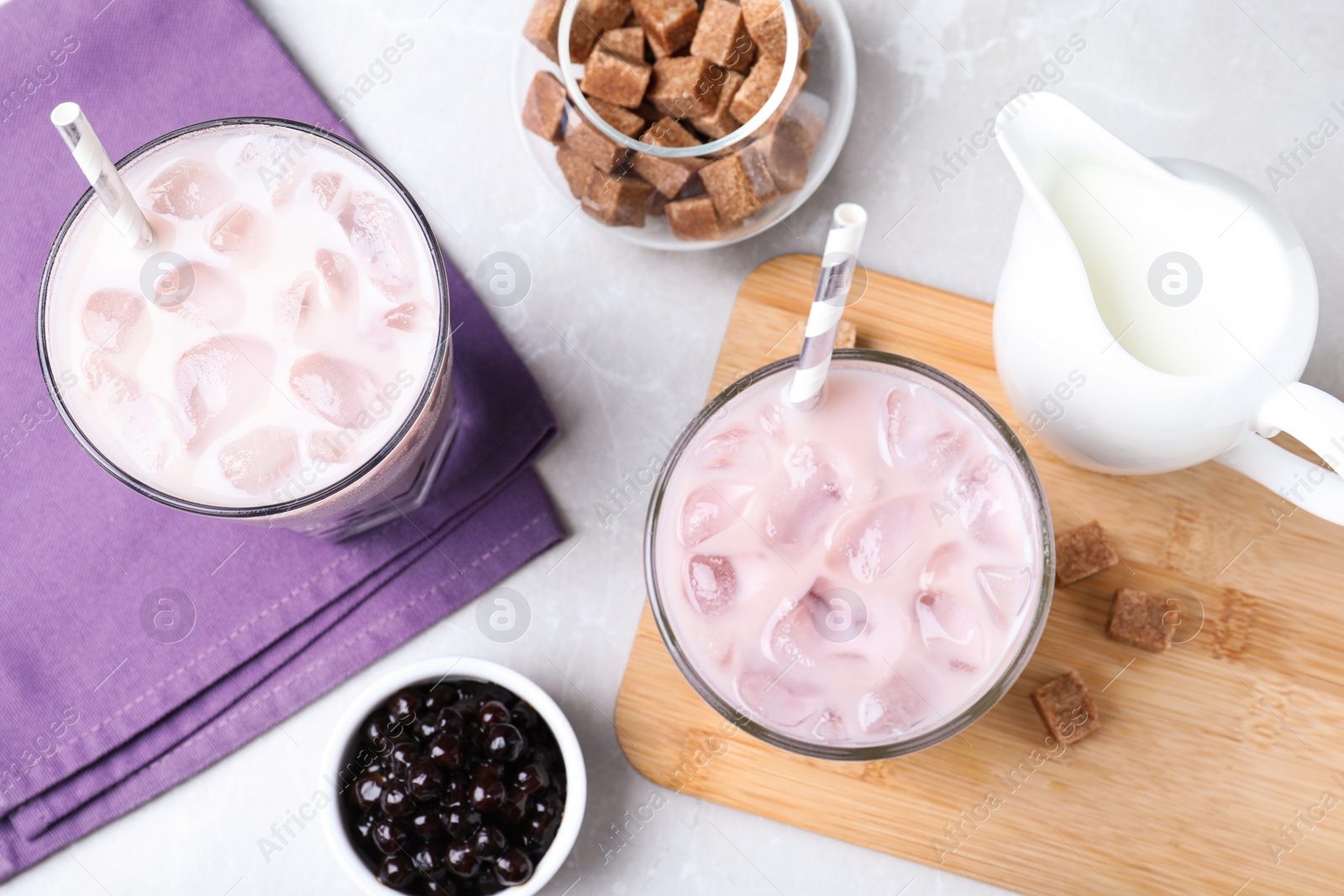 Photo of Bubble milk tea and bowl with tapioca balls on light grey marble table, flat lay