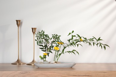 Photo of Stylish ikebana with beautiful yellow flowers, green branches and candlesticks carrying cozy atmosphere at home