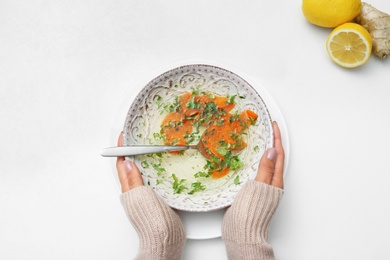 Photo of Woman with bowl of soup at white table, top view. Flu treatment