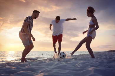 Friends playing football on beach at sunset