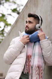 Handsome man in warm scarf and headphones near wall outdoors