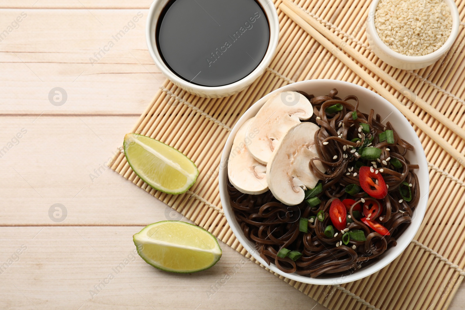 Photo of Tasty buckwheat noodles (soba) with mushrooms, onion and chili pepper served on wooden table, flat lay. Space for text