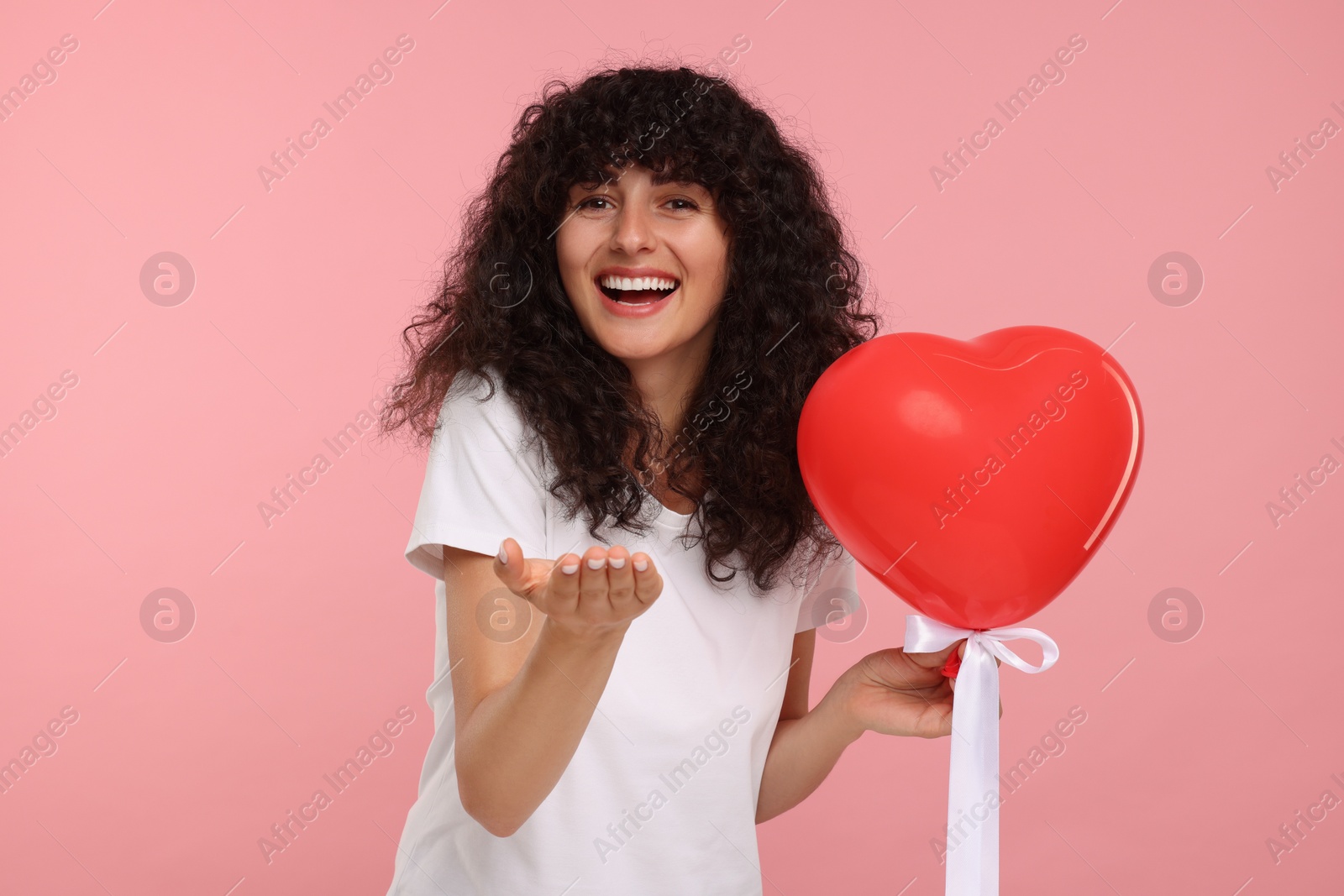 Photo of Young woman holding red heart shaped balloon on yellow background
