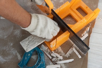 Photo of Worker cutting decorative wall tile indoors, closeup