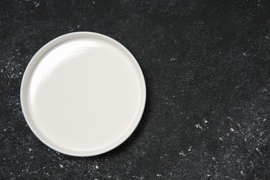 Photo of One ceramic plate on black textured table, top view. Space for text