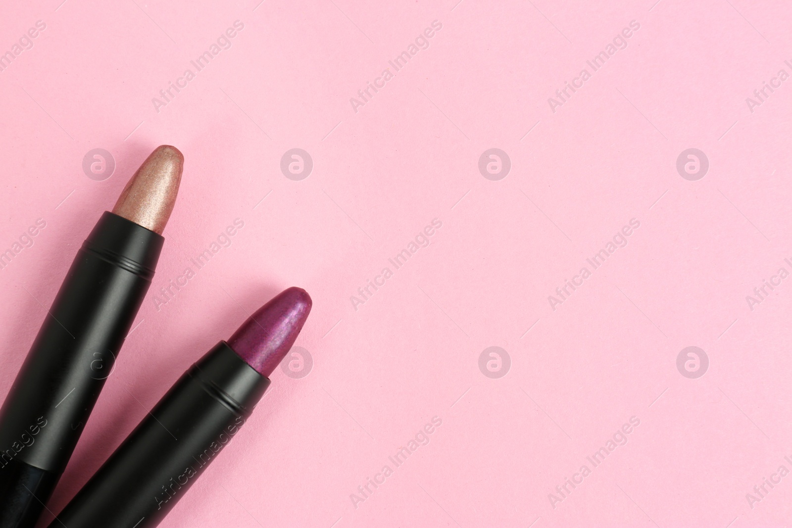 Photo of Bright lipsticks in black tubes on pink background, flat lay. Space for text