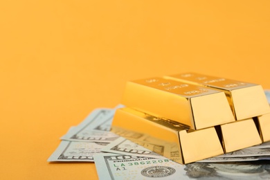 Photo of Shiny gold bars and dollar bills on color background. Space for text