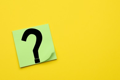 Photo of Sticky note with question mark on yellow background, top view. Space for text