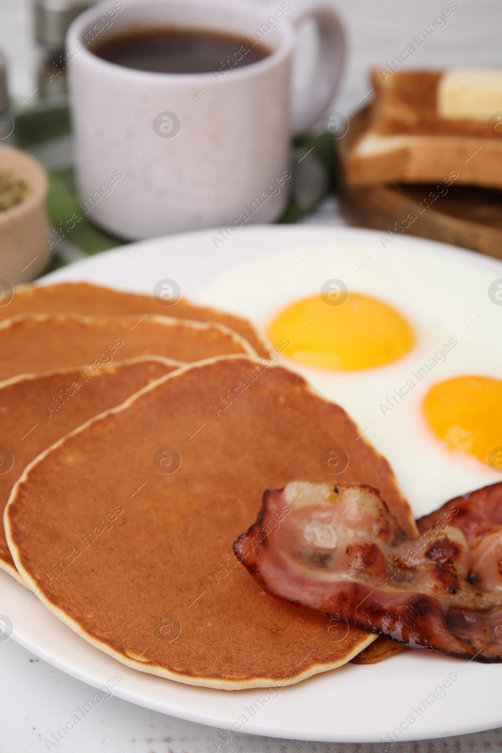 Photo of Tasty pancakes with fried eggs and bacon on white wooden table, closeup