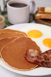 Photo of Tasty pancakes with fried eggs and bacon on white wooden table, closeup