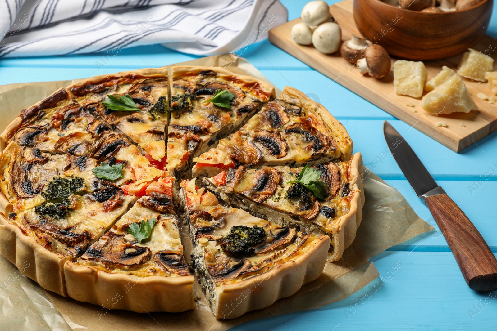 Photo of Delicious quiche with mushrooms and knife on light blue wooden table, closeup