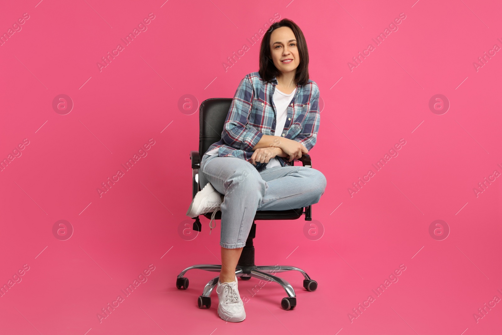 Photo of Mature woman sitting in comfortable office chair on pink background