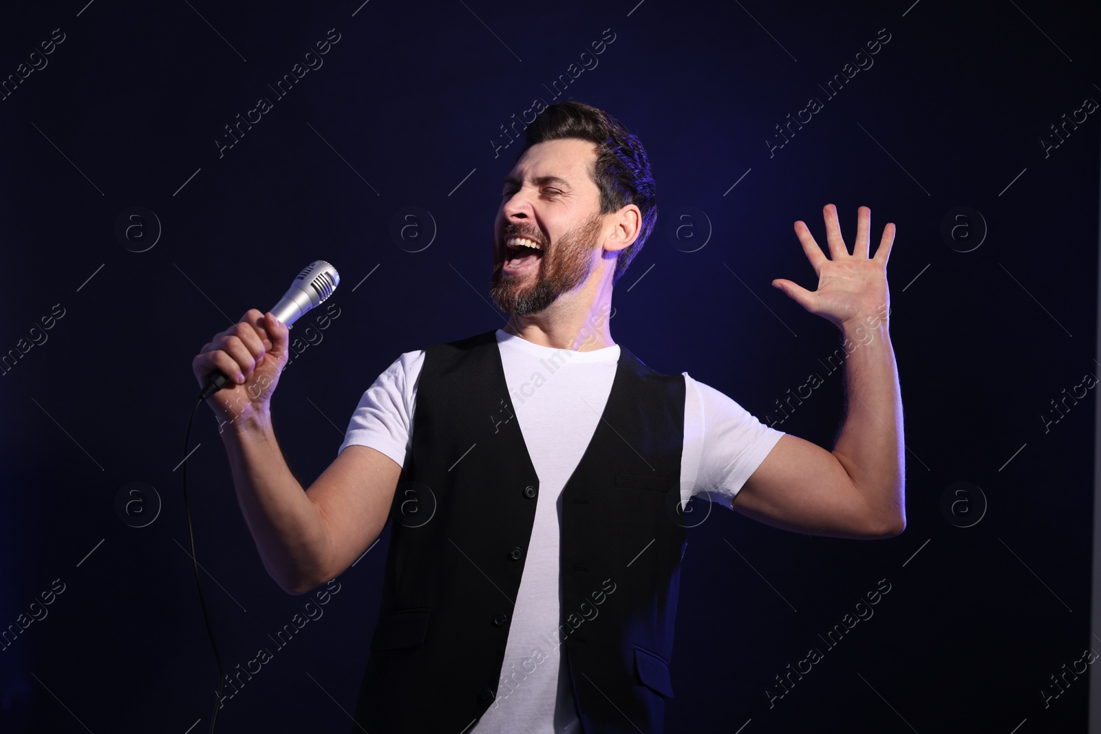 Photo of Handsome man with microphone singing on dark blue background