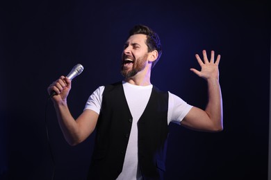 Handsome man with microphone singing on dark blue background