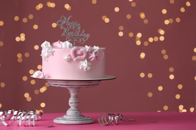 Photo of Beautifully decorated birthday cake on pink table against blurred festive lights, space for text