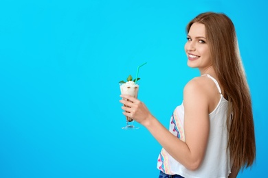 Young woman with glass of delicious milk shake on color background