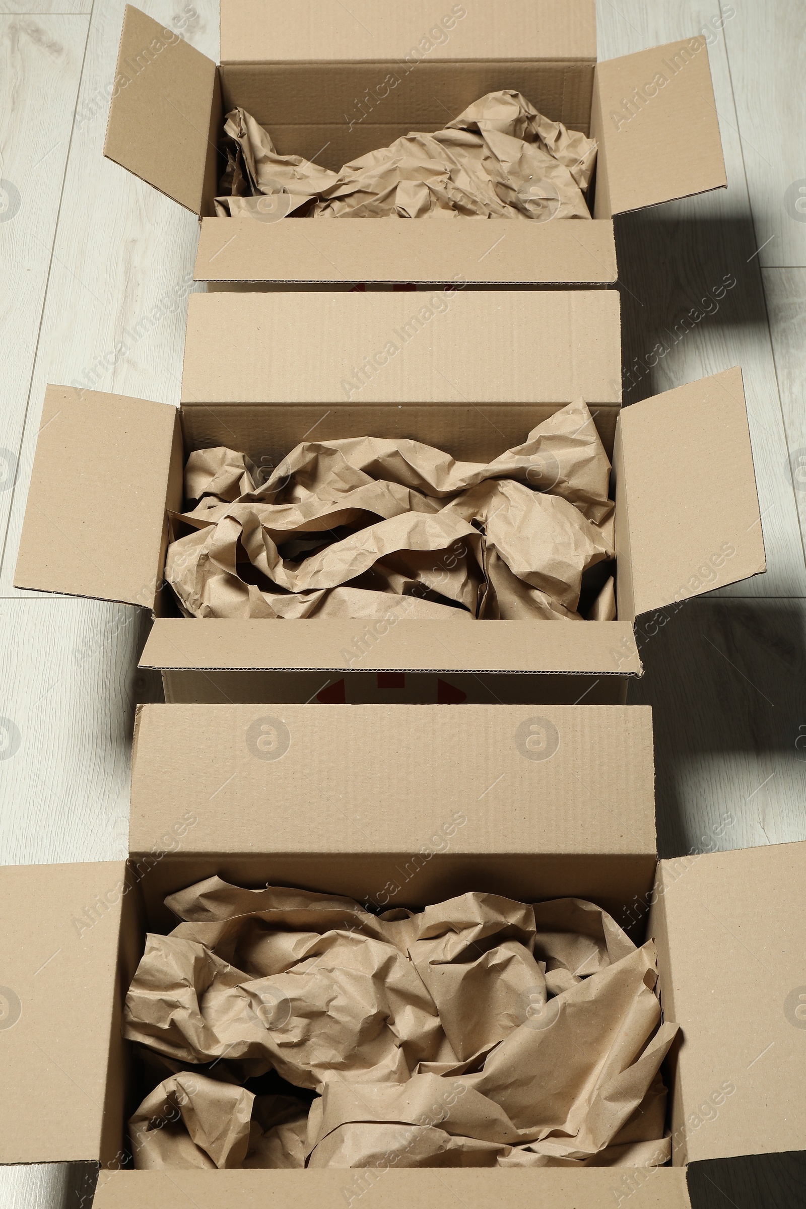 Photo of Open cardboard boxes with crumpled paper on white wooden floor