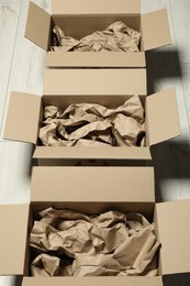 Open cardboard boxes with crumpled paper on white wooden floor