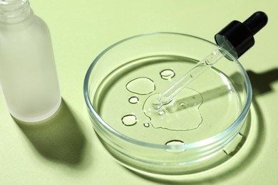 Photo of Petri dish with pipette and bottle on light green background
