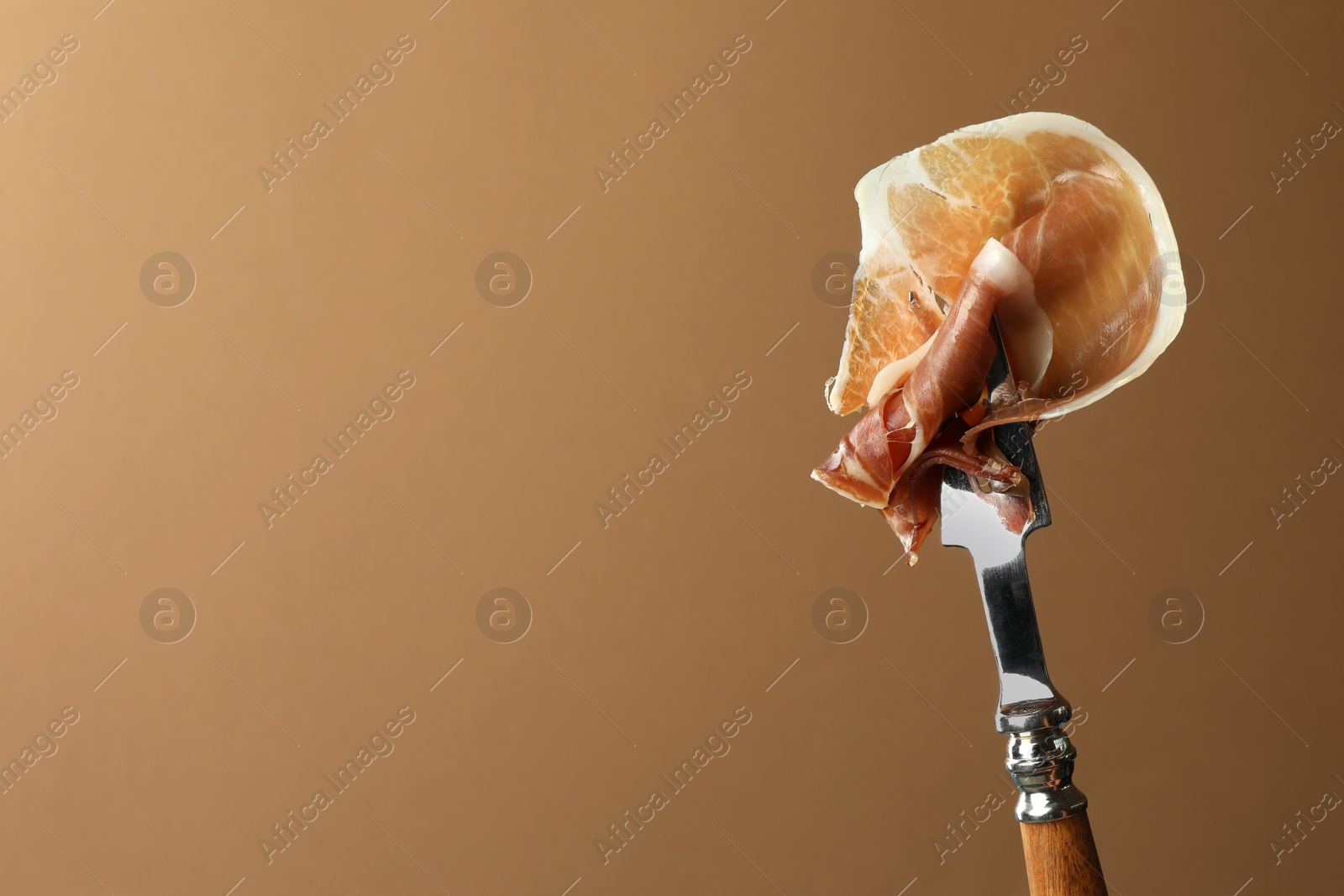 Photo of Fork with slice of tasty jamon on brown background, closeup. Space for text