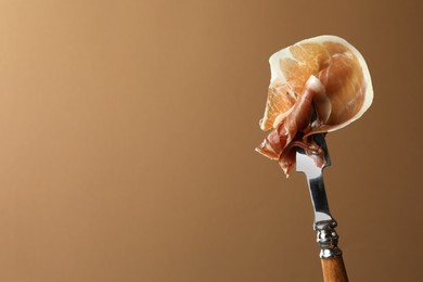 Photo of Fork with slice of tasty jamon on brown background, closeup. Space for text