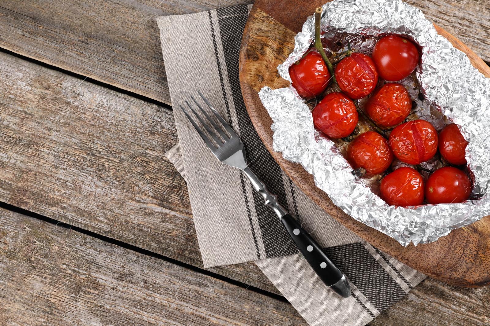 Photo of Aluminum foil with delicious baked tomatoes on wooden table, top view. Space for text