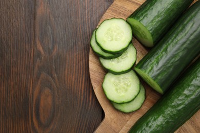 Photo of Fresh whole and cut cucumbers on wooden table, top view. Space for text