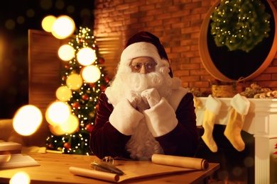 Photo of Santa Claus with wish list at table indoors