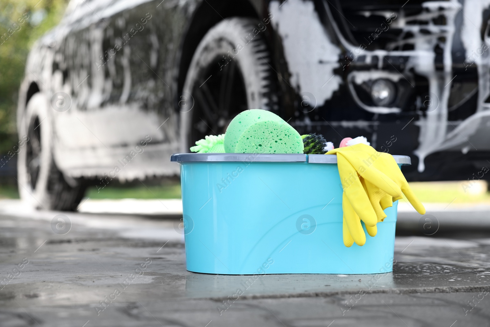 Photo of Car cleaning supplies and auto covered with foam outdoors