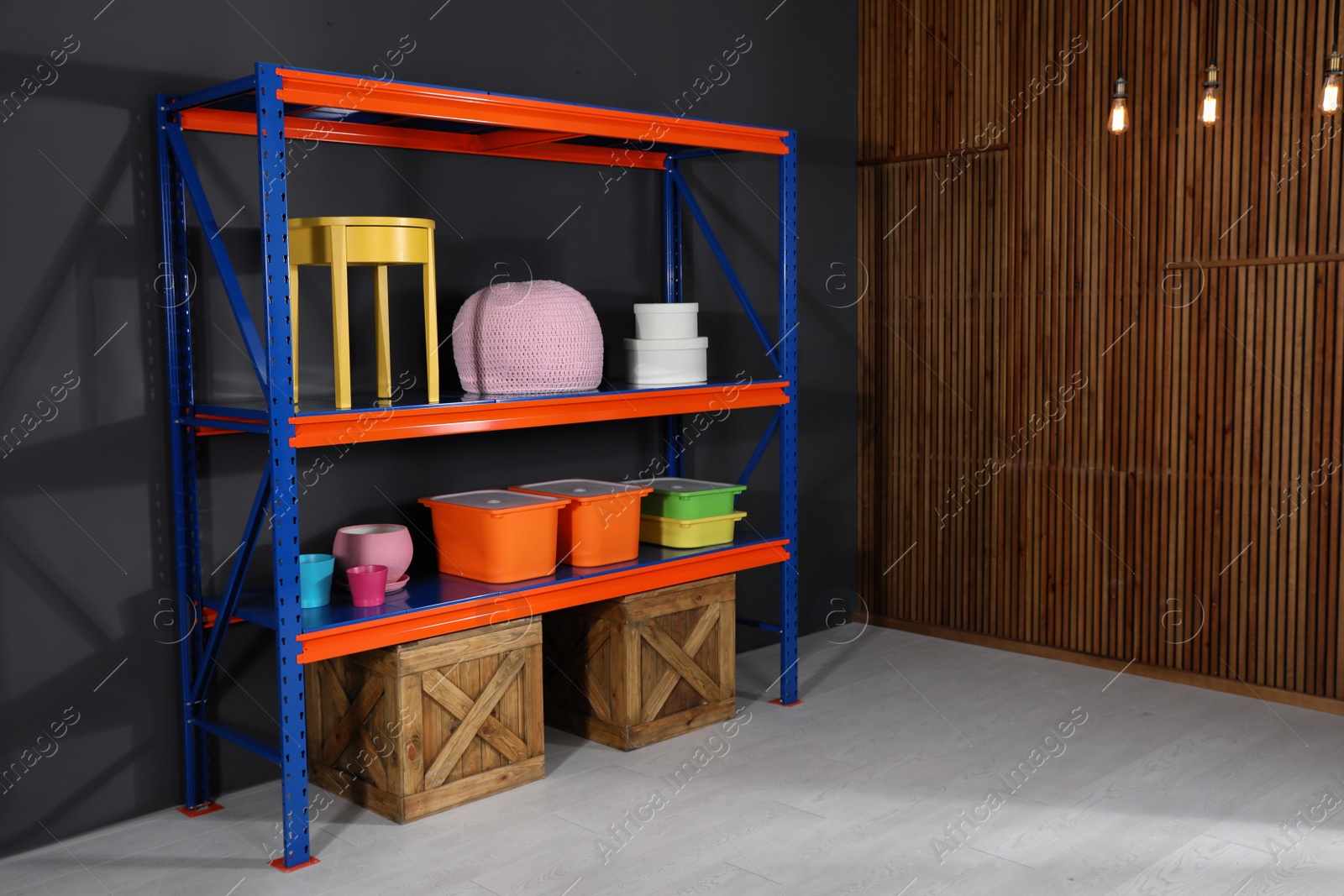 Photo of Metal shelving unit with wooden crates and different household stuff near black wall indoors. Space for text