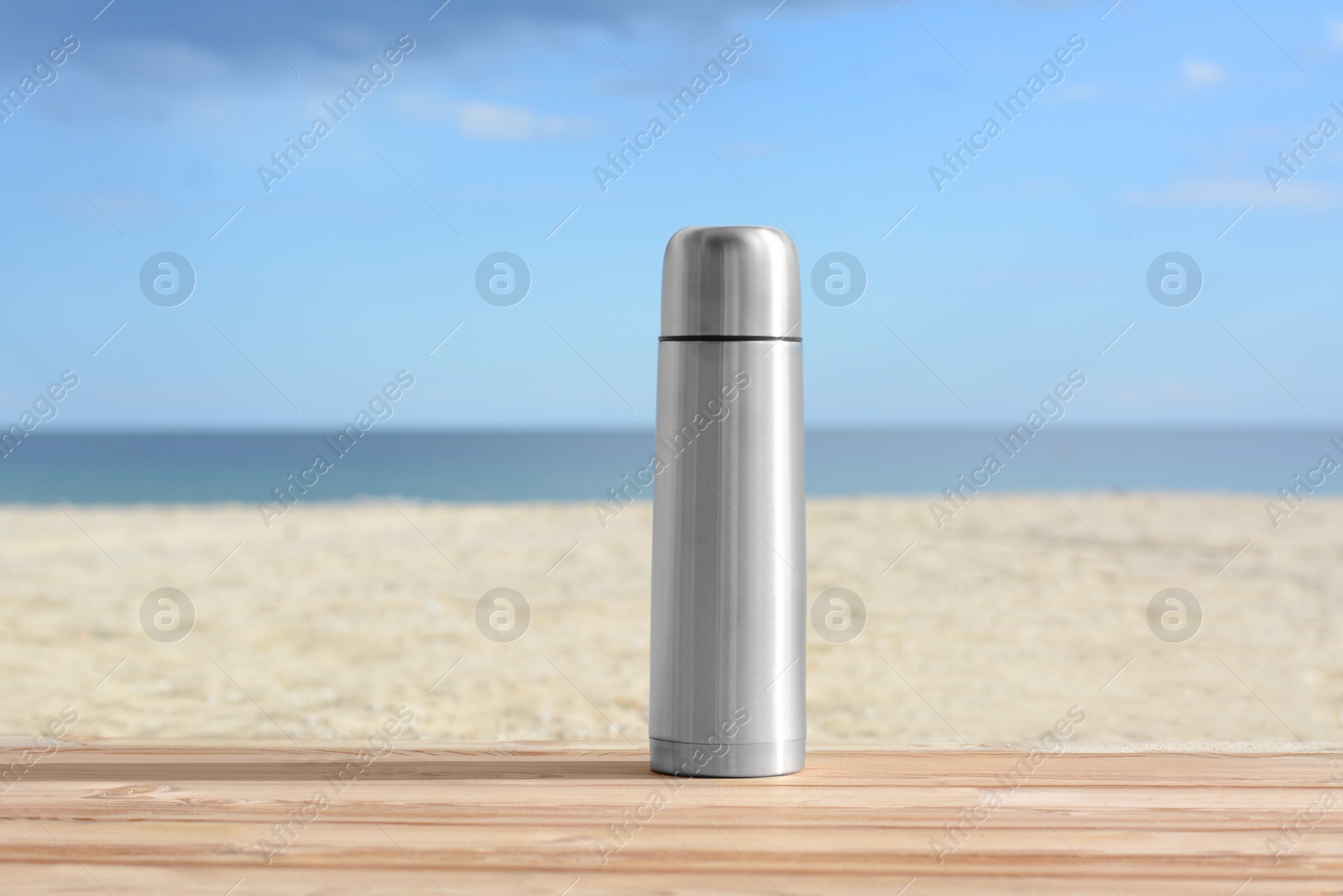 Photo of Metallic thermos with hot drink on wooden surface near sea, space for text