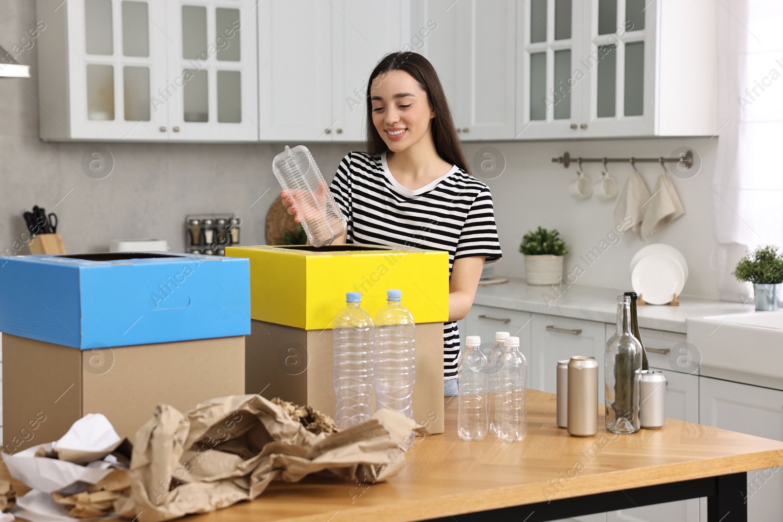 Photo of Smiling woman separating garbage at table in kitchen