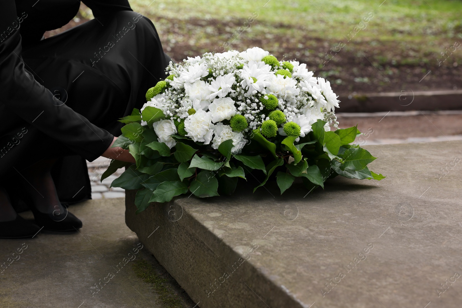 Photo of Woman with wreath of flowers near tombstone outdoors, closeup. Funeral attribute