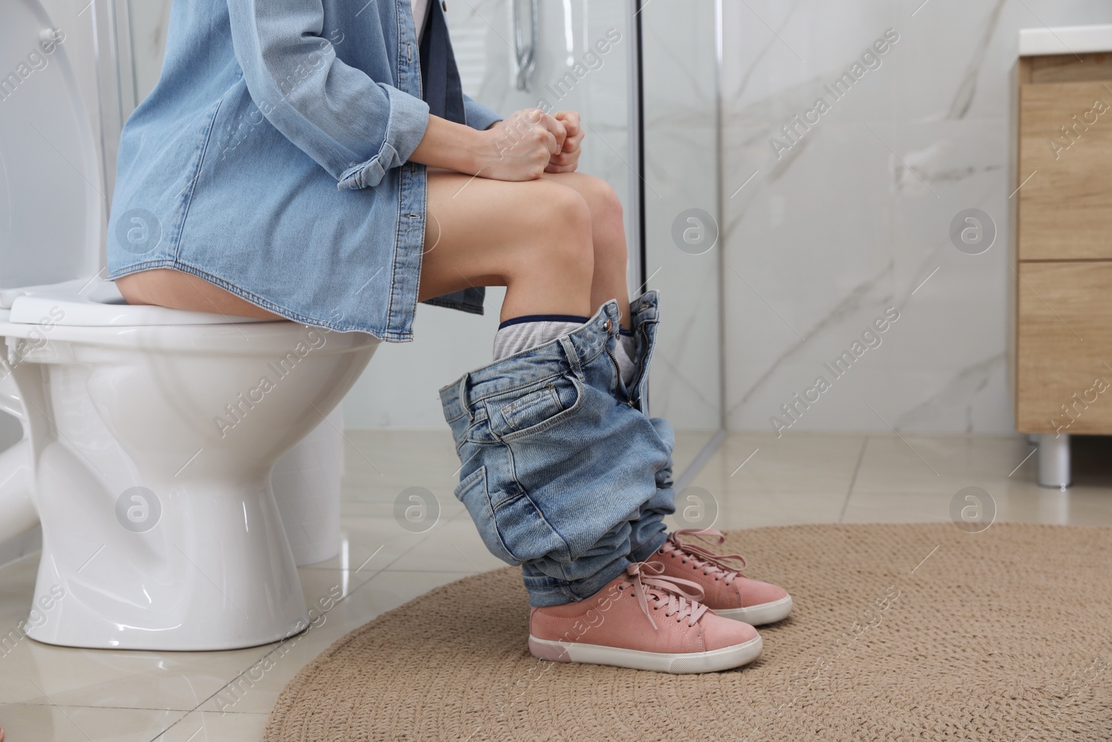 Photo of Woman suffering from hemorrhoid on toilet bowl in rest room, closeup