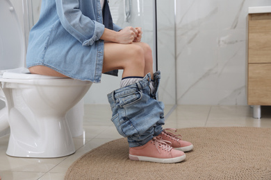 Woman suffering from hemorrhoid on toilet bowl in rest room, closeup