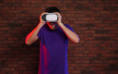 Emotional man playing video games with virtual reality headset near brick wall. Space for text