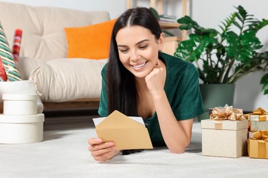 Photo of Happy woman reading greeting card on floor in living room