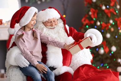 Authentic Santa Claus giving gift box to little girl indoors