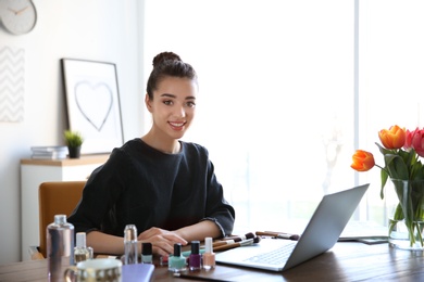 Young blogger with laptop and different cosmetics at table